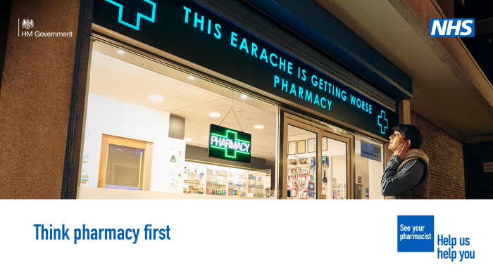 A person is standing outside a pharmacy holding the side of their face in discomfort. The sign above the pharmacy reads 